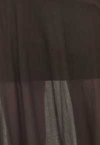 Gros plan sur un tissu léger marron foncé montrant des plis souples et une texture subtilement transparente.