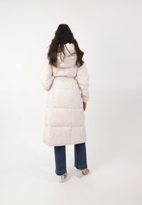 Abrigo acolchado largo en rosa claro con capucha y cinturón, con un diseño acolchado. Combinado con jeans de mezclilla acampanados y sandalias de tacón transparente.