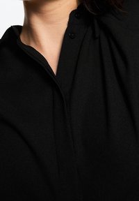 Black shirt with a collar, featuring buttons at the neckline. The fabric appears soft with a smooth texture and subtle draping.