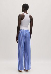 Witte mouwloze tanktop en blauw gestreepte wijde broek. De strepen zijn verticaal, de broek heeft een ontspannen pasvorm en een elastische tailleband.
