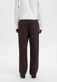 Mørkebrune vide bukser med to baklommer, kombinert med en hvit langermet skjorte. Materialet virker mykt med en lett teksturert overflate.