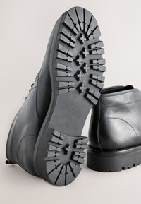 Schwarze Lederstiefel mit einer robusten, strukturierten Gummisohle und tiefem Profil für guten Halt. Glatte Oberseite mit dezenten Nähten.