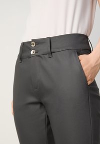 Black trousers with two metal buttons at the waist, front pockets, and a smooth, sleek fabric texture. Tailored fit highlighted.
