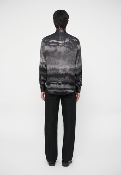 Langarm overhemd in zwart en grijs met een gestructureerd, abstract patroon. Gecombineerd met losse zwarte broek en zwarte schoenen.