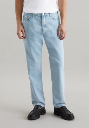 Light blue straight-leg jeans made of denim, featuring five pockets and a button closure. Worn with black loafers and a white t-shirt.