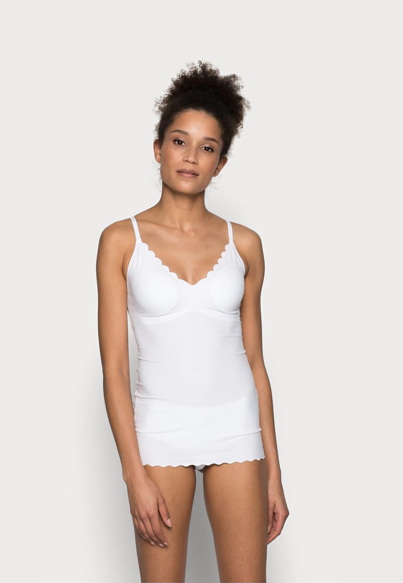 White camisole with scalloped edges, adjustable straps, and a fitted design. Made from smooth, stretchy fabric for comfort.