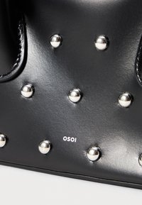 Juodas odinės rankinės, puoštos sidabriniais metaliniais kniedėmis ir spausdintu logotipu "OSOI". Lygus paviršius, su apvaliomis formomis ir kontrastingomis medžiagomis.