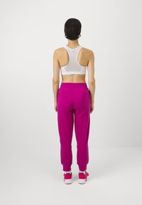 Biały sportowy crop top z siateczkowym tyłem, zestawiony z różowymi dresowymi spodniami. Spodnie mają ściągacze przy kostce oraz boczne kieszenie.