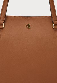 Bolsa tote sintética castanha com textura em relevo, logotipo em tom de ouro e asas superiores com ferragens de metal. Design simples e elegante.