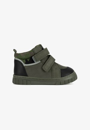 Zapatilla de deporte para niño pequeño en verde y negro con tejido de camuflaje, doble cierre de velcro y suela de goma texturizada.