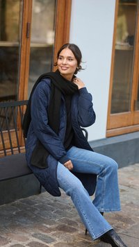 Marineblå quiltet lang frakke med et sort tørklæde, båret over en sort top og lyseblå flared jeans. Sorte ankelstøvler fuldender outfittet.