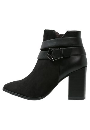 Botines negros con un upper de cuero mate y un panel de ante texturizado. Tienen una punta afilada, un tacón grueso y alto, y una correa con un detalle de herrajes.