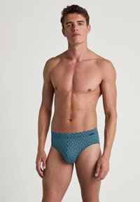 Blauwe zwemslip met een geometrisch patroon, gemaakt van rekbaar materiaal. Soepele textuur met een lage taille.