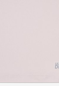 Light pink mesh fabric with a textured pattern; features subtle branding in gray at the bottom right. Soft material, breathable design.