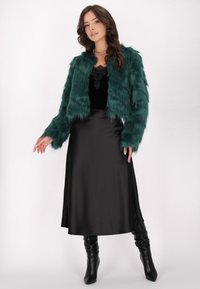 Jachetă din blană sintetică teal cu un design scurt, asociată cu o fustă neagră din satin. Modelul poartă cizme negre cu toc până la genunchi.