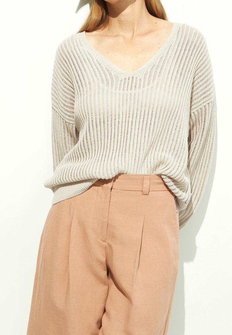 Pull tricoté beige clair avec encolure en V et texture côtelée, associé à un pantalon taille haute rose clair. Coupe décontractée avec épaules tombantes.