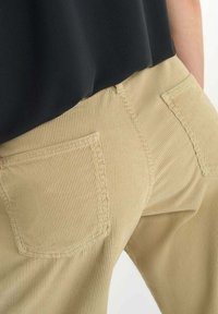 Beige corduroy broek van textuurstof, met twee achterzakken en een rechte pasvorm, gedragen met een zwart top.