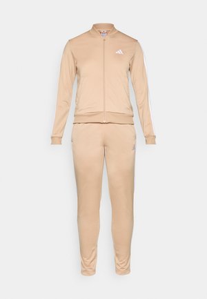 Beige treningsdrakt laget av glatt stoff, med en glidelåsjakke med høy krage og matchende bukser med hvite sidestriper og logo.