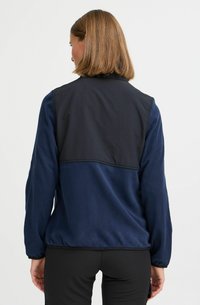 Veste en polaire bleu marine avec des panneaux noirs ; tissu texturé, manches longues et poignets élastiques. Conçue pour le confort et la chaleur.