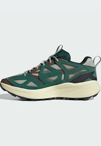 La sneaker presenta una toma in mesh verde con accenti marroni, un sistema di lacci rinforzato, una suola intermedia spessa di colore crema e una suola esterna nera robusta.