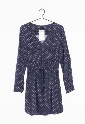 Navyblaues Kleid mit langen Ärmeln, V-Ausschnitt, zwei Brusttaschen, elastischem Taillengummi mit Bindeband und einem Rautenmuster über das gesamte Kleid.
