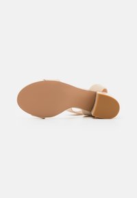 Beige sandaalit korkealla korolla, joissa on sileä nahkapäällinen, leveä nilkkanauha ja kumipohja. Varustettu lohkarekorolla ja teksturoidulla pohjalla pidon parantamiseksi.