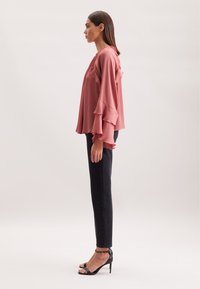 Blusa rosa con maniche a volant, abbinata a jeans neri aderenti e tacchi alti neri a fascia. Tessuto morbido e design fluido.