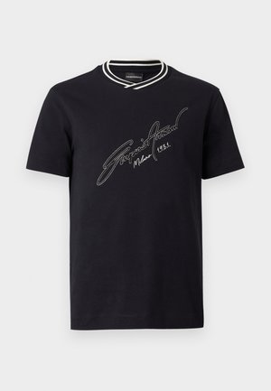Crna majica kratkih rukava s bijelim prugastim rebrastim okovratnikom i bijelim tekstom u stilu potpisa "Emporio Armani Milano 1981" na prsima.