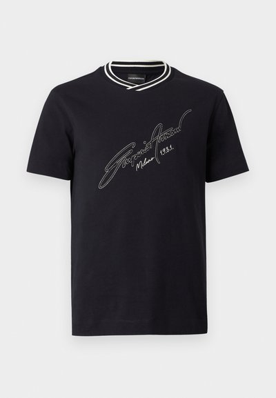 Crna majica kratkih rukava s bijelim prugastim rebrastim okovratnikom i bijelim tekstom u stilu potpisa "Emporio Armani Milano 1981" na prsima.