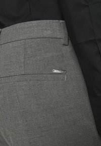 Pantaloni grigi realizzati in un tessuto testurizzato con una vestibilità slim. Presentano una tasca posteriore e un'etichetta logo argento. Si abbinano a una parte superiore nera.