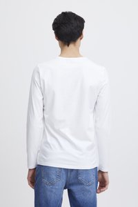 Hosszú ujjú fehér pamut póló környakkivágással, sima textúrával és tiszta varratokkal, kék farmernadrággal, melyen hátul zsebek találhatók.