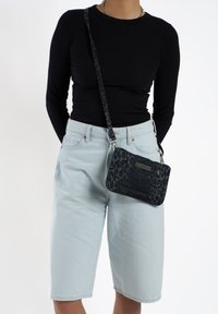 Kleine zwarte crossbody tas met luipaardprint, voorzien van een textuurafwerking en een zilveren accent. Verstelbare schouderband en ritsafsluiting.