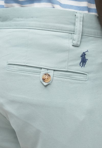 Ανοιχτό μπλε βαμβακερό παντελόνι με πίσω τσέπη που κλείνει με καφέ κουμπί και σκούρο μπλε κεντημένο λογότυπο με έναν ιππέα.