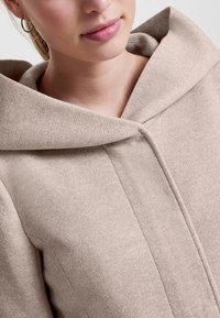Beige ullblandingskjole med stor hette, lukket med en diskret knapp, med en myk og teksturert finish.