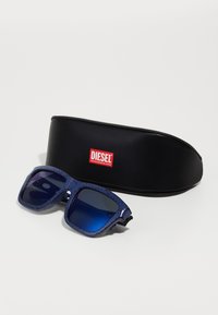 Óculos de sol azul marinho com uma armação texturizada e lentes azuis com gradiente, acompanhados de um estojo protetor preto com o logotipo vermelho da Diesel.