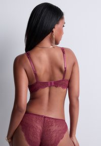 Bralette en dentelle bordeaux avec des bretelles ajustables et une fermeture à crochets. Associé à une culotte en dentelle transparente assortie avec un motif floral.