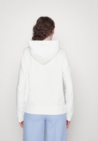Sudadera blanca con capucha grande y suave, puños acanalados y dobladillo recto. La tela parece lisa con un diseño limpio y minimalista.