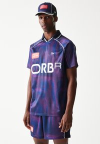 Αθλητική φανέλα και σορτς με μοτίβο σε αποχρώσεις του μωβ και μπλε, με λευκές λεπτομέρειες και λογότυπα. Το υλικό είναι διαπνέον και το σχέδιο περιλαμβάνει V-λαιμόκοψη.