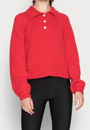 Rode gebreide trui met lange mouwen, kraag en drie decoratieve knopen, gecombineerd met zwarte strakke broek.