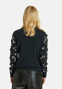 Czarny sweter z dzianiny z ozdobnymi wzorami kwiatowymi i cekinami na rękawach. Ribbowane wykończenie dołu i mankietów, w zestawie z czarnymi skórzanymi spodniami.