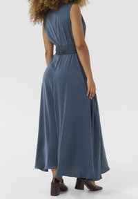 Bla dressesimaxikleid ohne Ärmel mit einem gebundenen Taillenband, weichem Stoff, fließendem Rock und glatter Textur. Kombiniert mit burgunderfarbenen Blockabsatzschuhen.