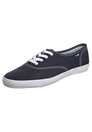 Baskets en toile noire avec lacets et semelle blanches, design bas, coutures blanches visibles et petit logo Keds sur le côté.