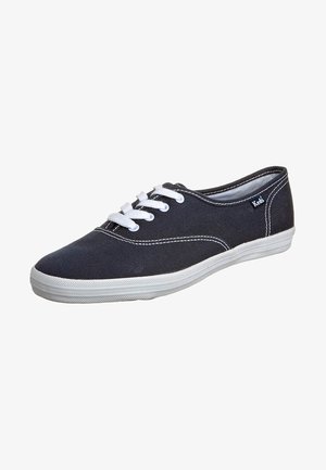 Baskets en toile noire avec lacets et semelle blanches, design bas, coutures blanches visibles et petit logo Keds sur le côté.