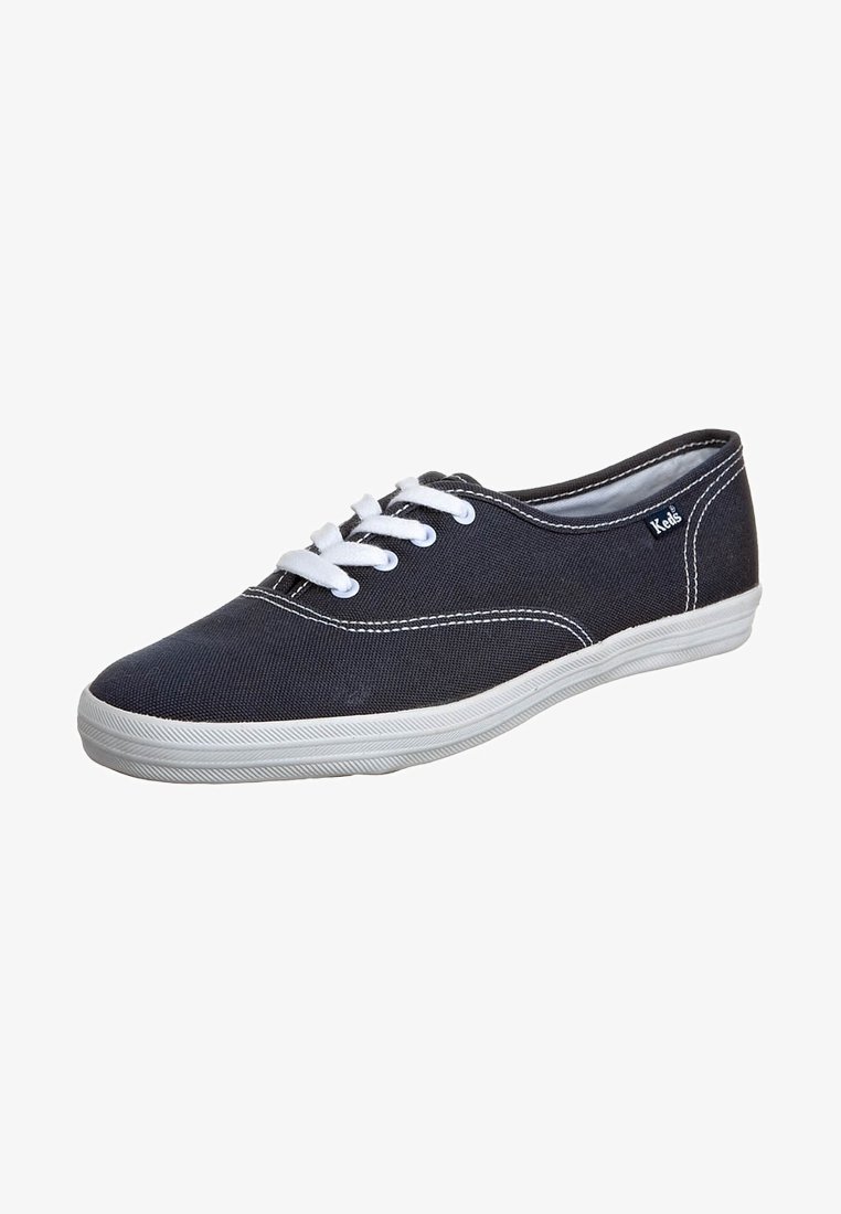 Baskets en toile noire avec lacets et semelle blanches, design bas, coutures blanches visibles et petit logo Keds sur le côté.