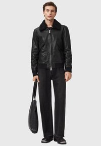 Sort læder bomberjakke med en pelskrave i shearling, kontrasterende ribstrikkede manchetter, båret med løstsiddende sorte denimbukser og en sort tote-taske.