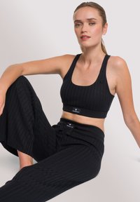 Brassière de sport noire côtelée et pantalon large assorti, avec un logo sur la bande et un tissu texturé pour plus de confort et de flexibilité.