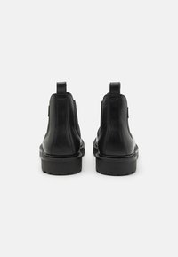Bottines noires en cuir avec des panneaux latéraux élastiques, des tirettes et des semelles en caoutchouc épaisses, présentant une texture lisse et une forme arrondie.