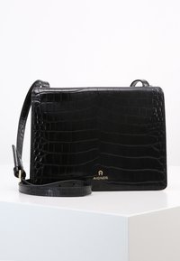 Borsa a mano in pelle nera con texture a coccodrillo, forma rettangolare, dettagli in oro e tracolla regolabile. Logo Aigner presente sul fondo.