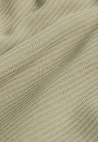 Detailný záber béžovej rebrovanej pleteniny so zvýraznenými vertikálnymi líniami a jemnými záhybmi.