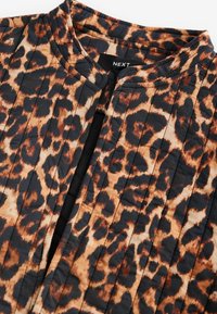 Gros plan d'une veste matelassée avec un motif léopard marron et noir et un col rond sans boutons ni fermeture éclair visibles.